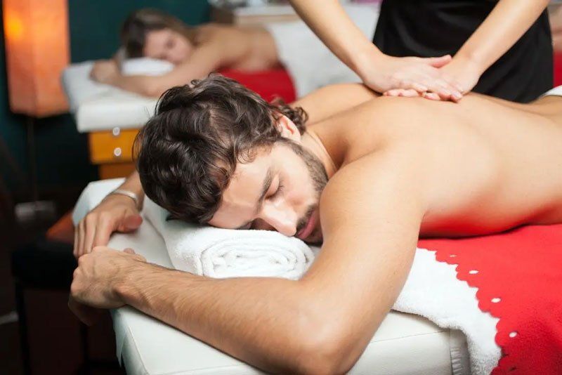 A person receives a back massage while lying on a table in a spa, with another person resting on a table in the background.