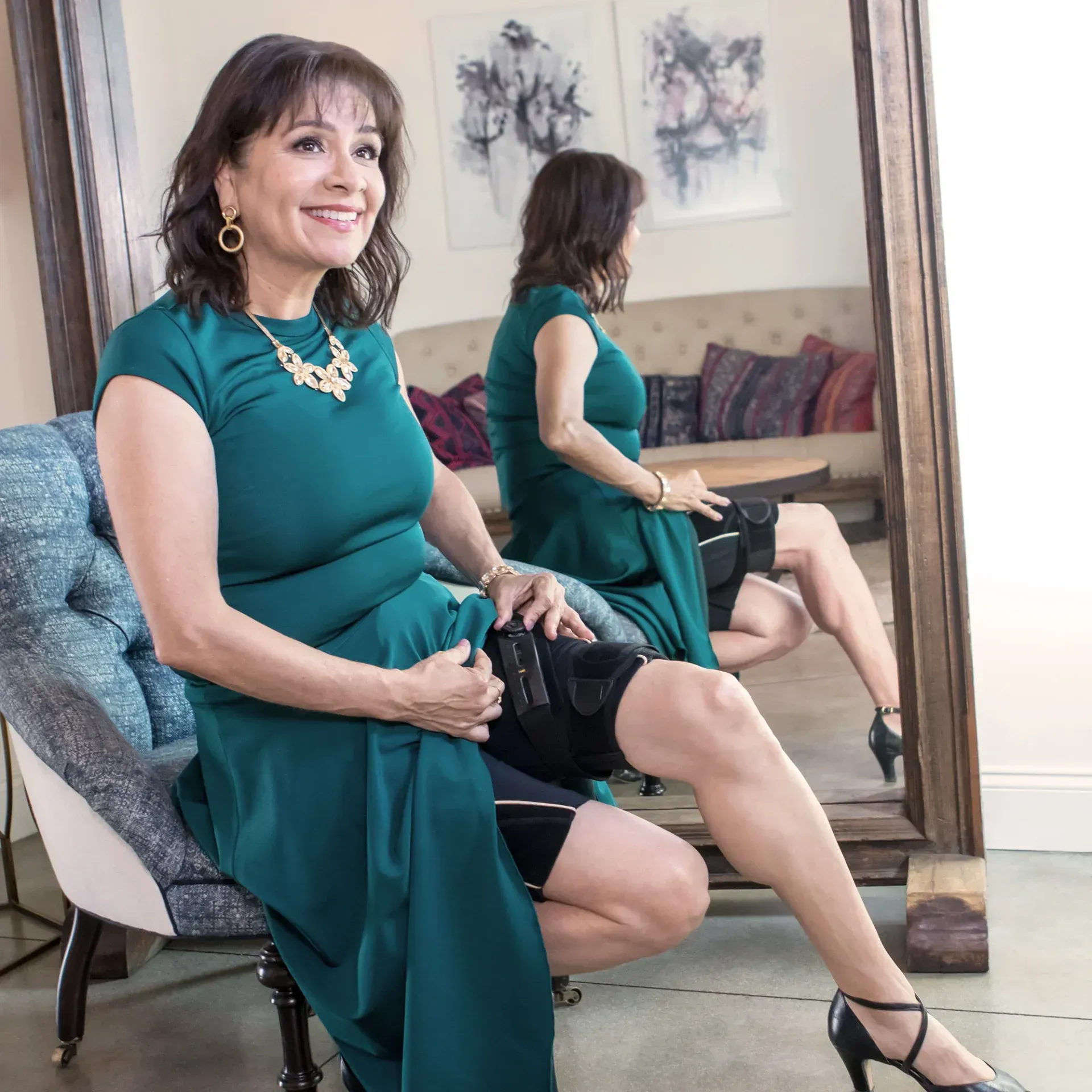 A person in a green dress sits on a chair, lifting their skirt to reveal a concealed thigh holster for a firearm.
