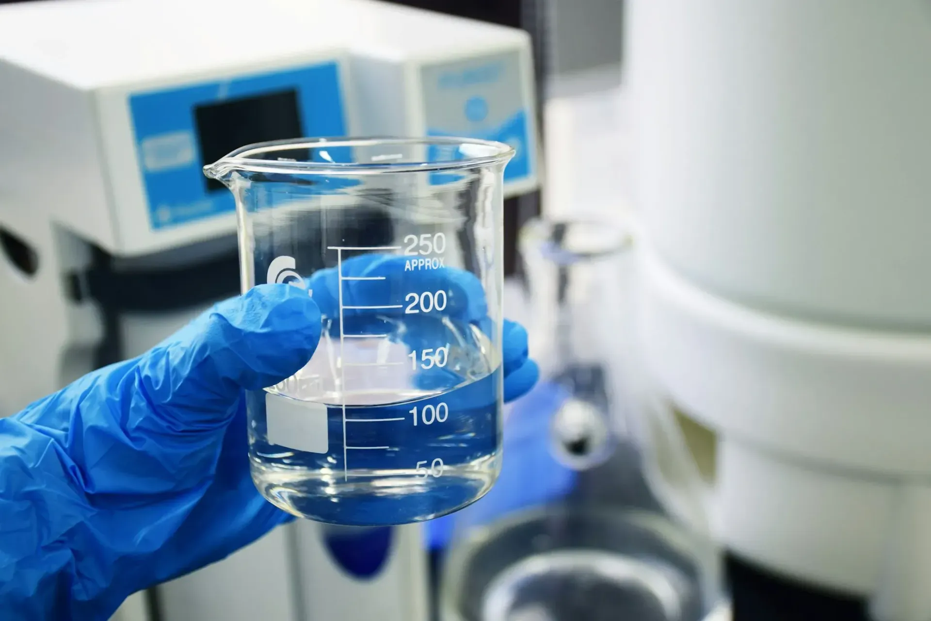 A person wearing blue gloves is holding a beaker filled with liquid.