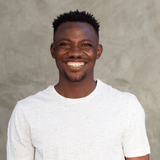 A man with a beard is wearing a white t-shirt and smiling.
