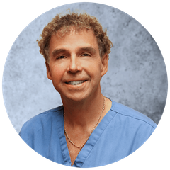 A man in a blue scrub top is smiling for the camera