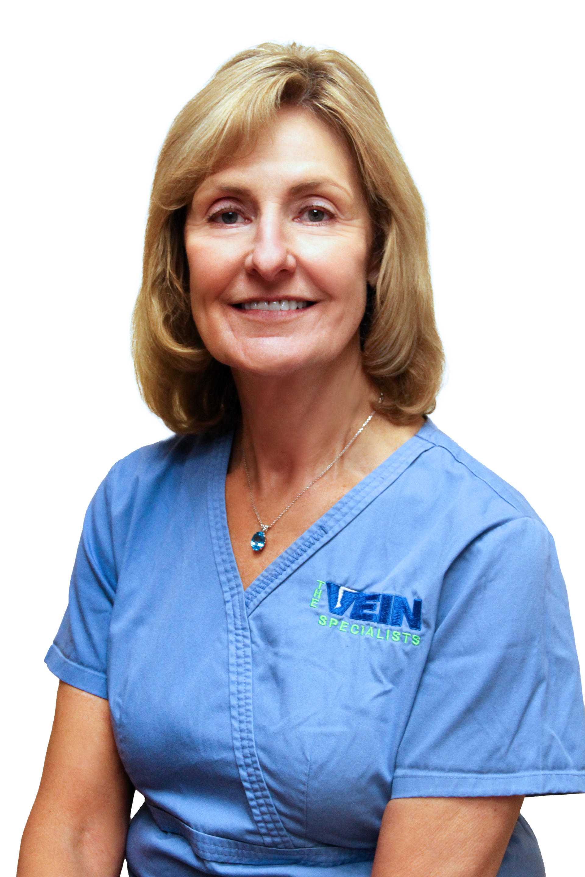 A woman in blue scrubs wearing a necklace smiling.