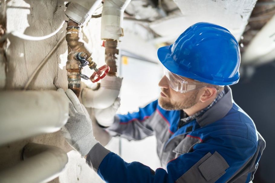 Technician in blue hard hat inspecting industrial pipes and valves in a maintenance area