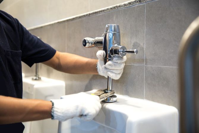 Gloved hands cleaning a chrome faucet over a white sink in a tiled restroom.