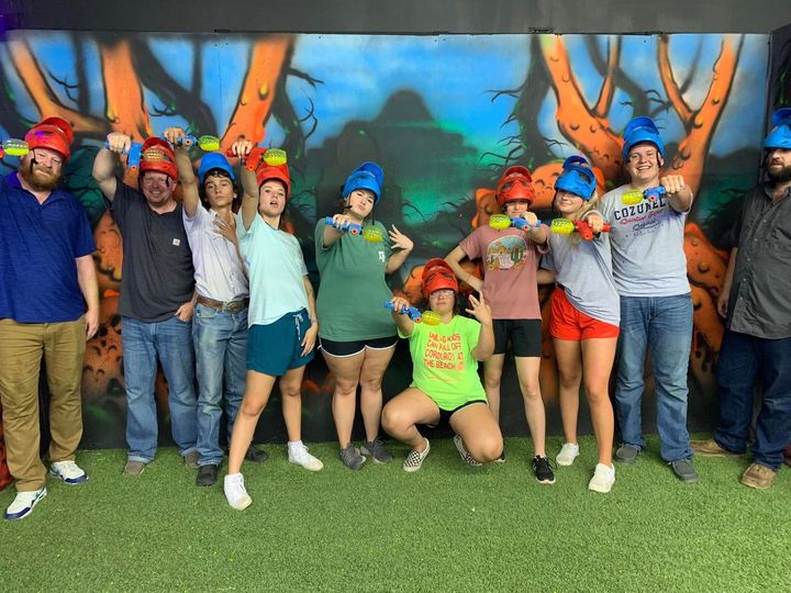 Group of people posing together in colorful shirts and hats in front of a painted mural.