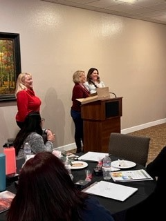 Three women are standing at a podium giving a presentation to a group of people.