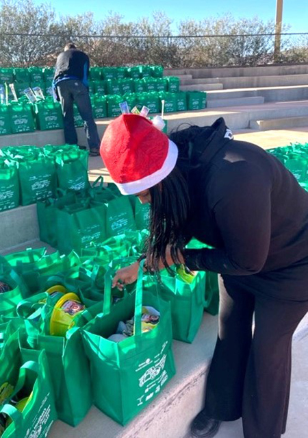 A woman wearing a santa hat reaches into a green bag