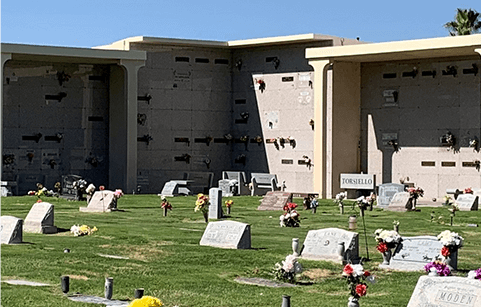 A cemetery with lots of graves and flowers in front of a large building.