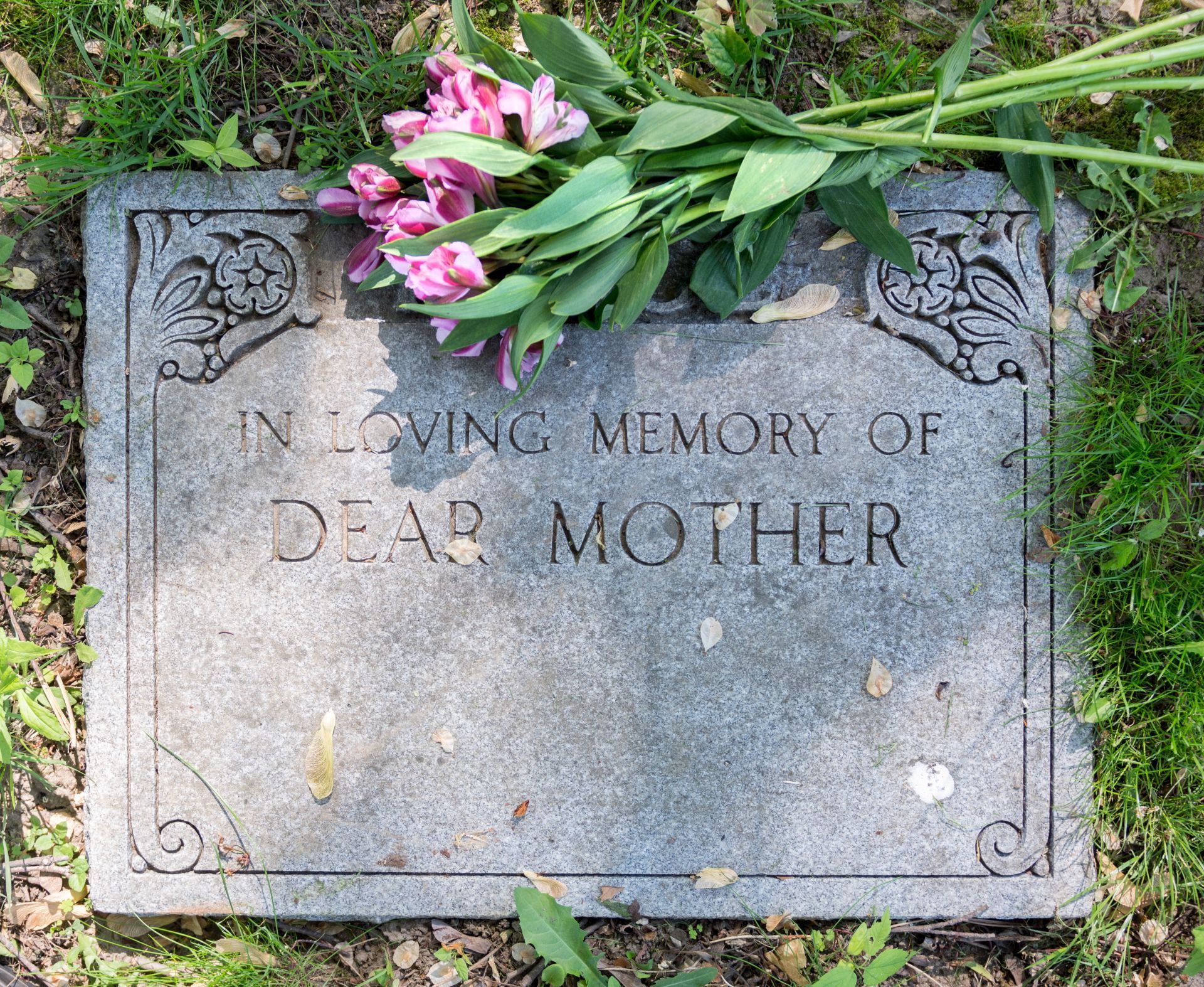 A gravestone with flowers on it that says in loving memory of dear mother