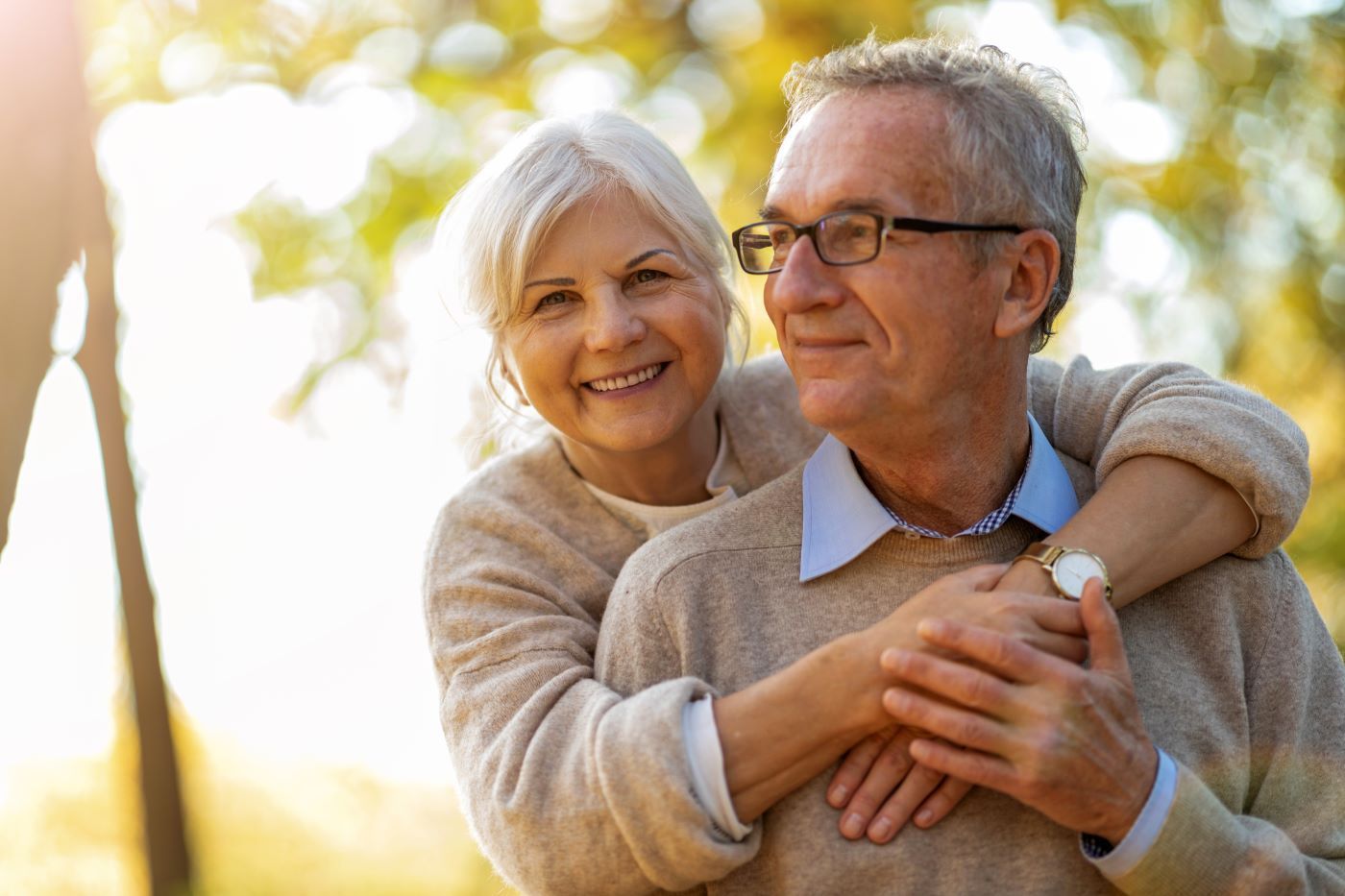 An elderly couple is hugging each other in a park.