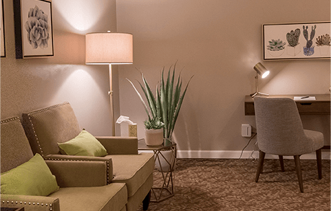 A living room with a couch , chair , desk and lamp.