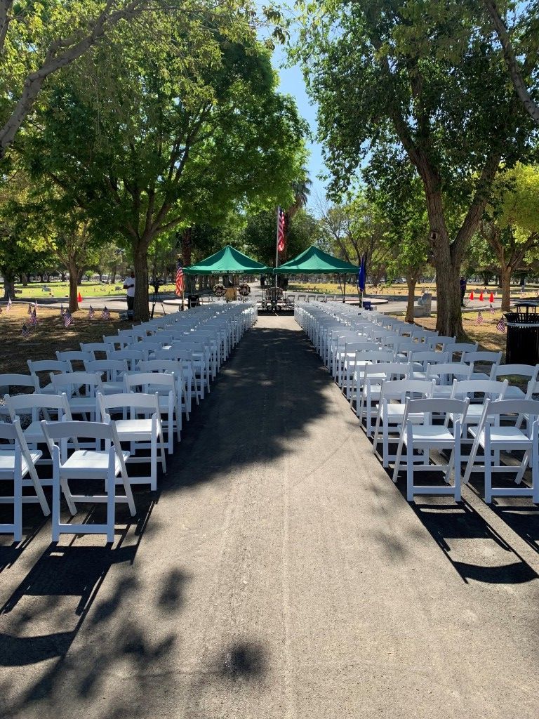 A row of white folding chairs are lined up in a park