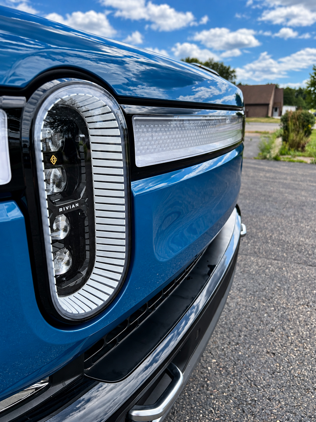 Close-up of a blue car’s front light and grille on a paved roadside.
