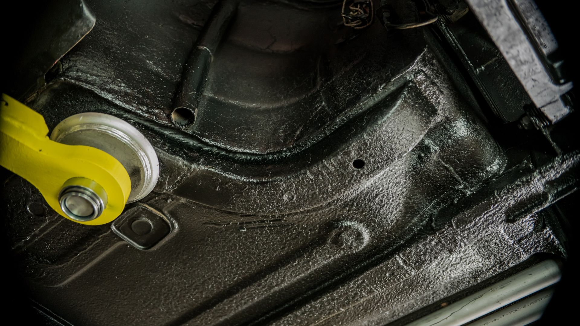 Yellow suspension bushing mounted under a car chassis with dark metal frame and undercoating