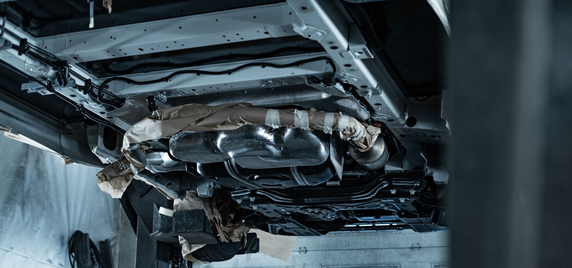 Undercarriage of a car with damaged exhaust and chassis parts, viewed from below in a garage-like setting