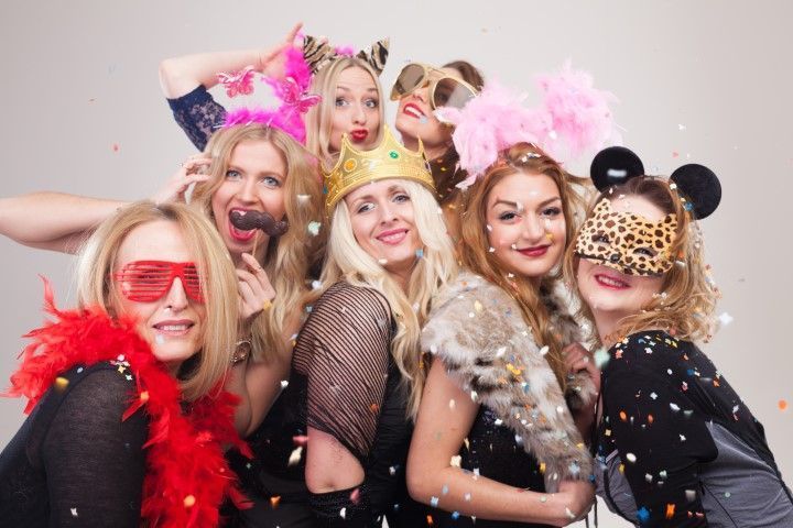 Group of people in colorful costumes and feather boas posing closely together at a party, smiling at the camera
