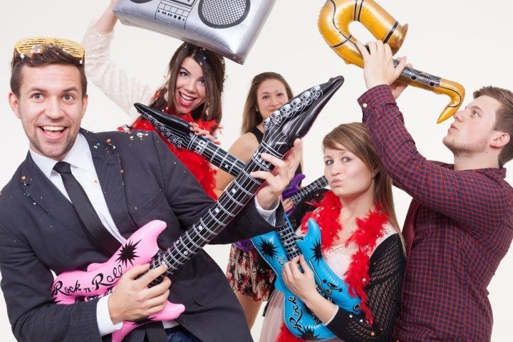 People posing with colorful inflatable guitars and a boombox, smiling in a lively studio scene