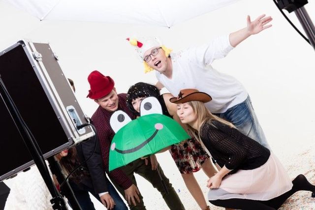 Four people posing playfully in costumes against a white background, one holding a green umbrella props