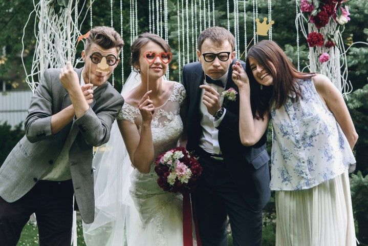 Four people posing playfully in front of a floral wedding backdrop, making peace signs and smiling.