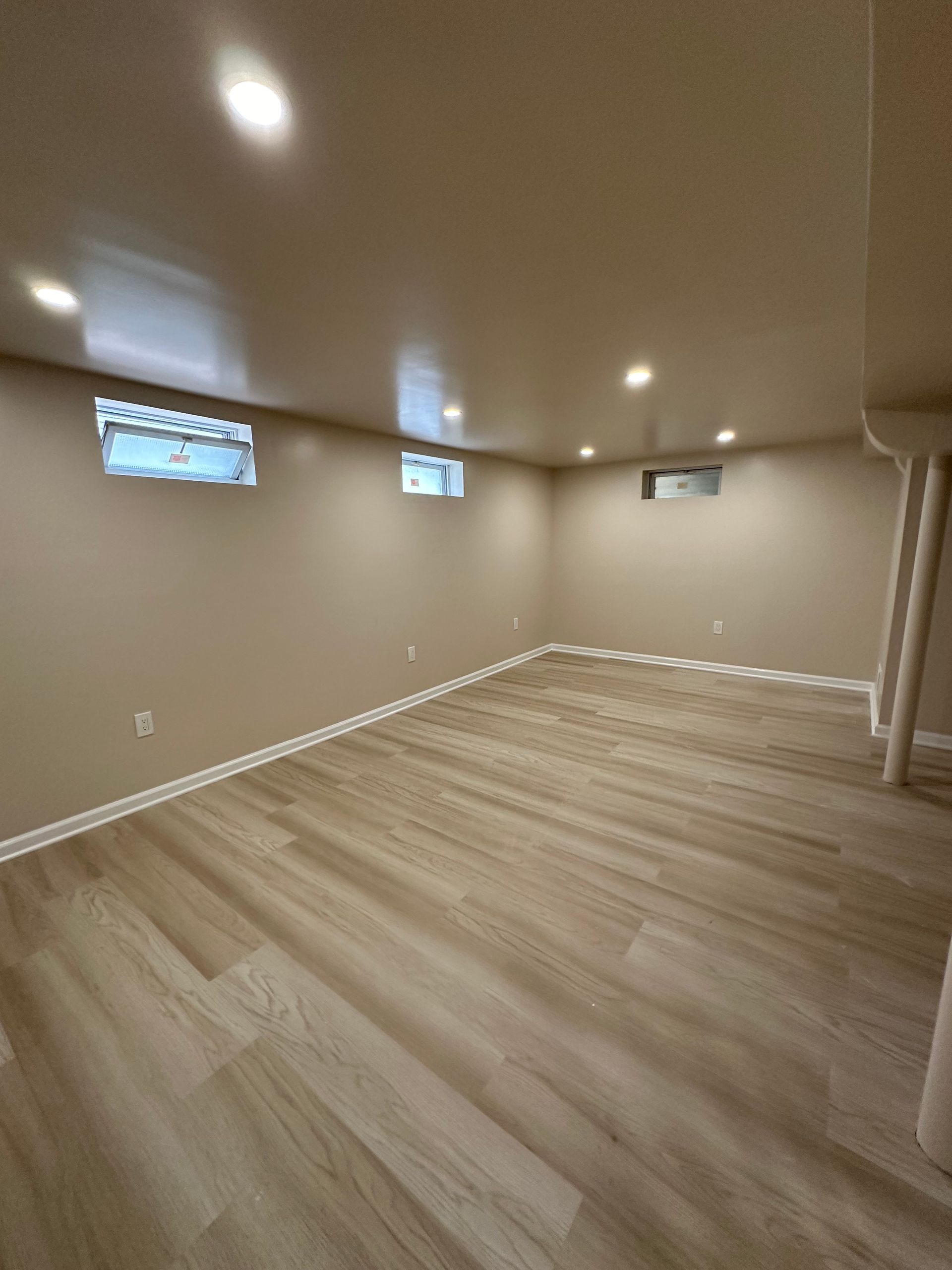 An empty basement with hardwood floors and beige walls.
