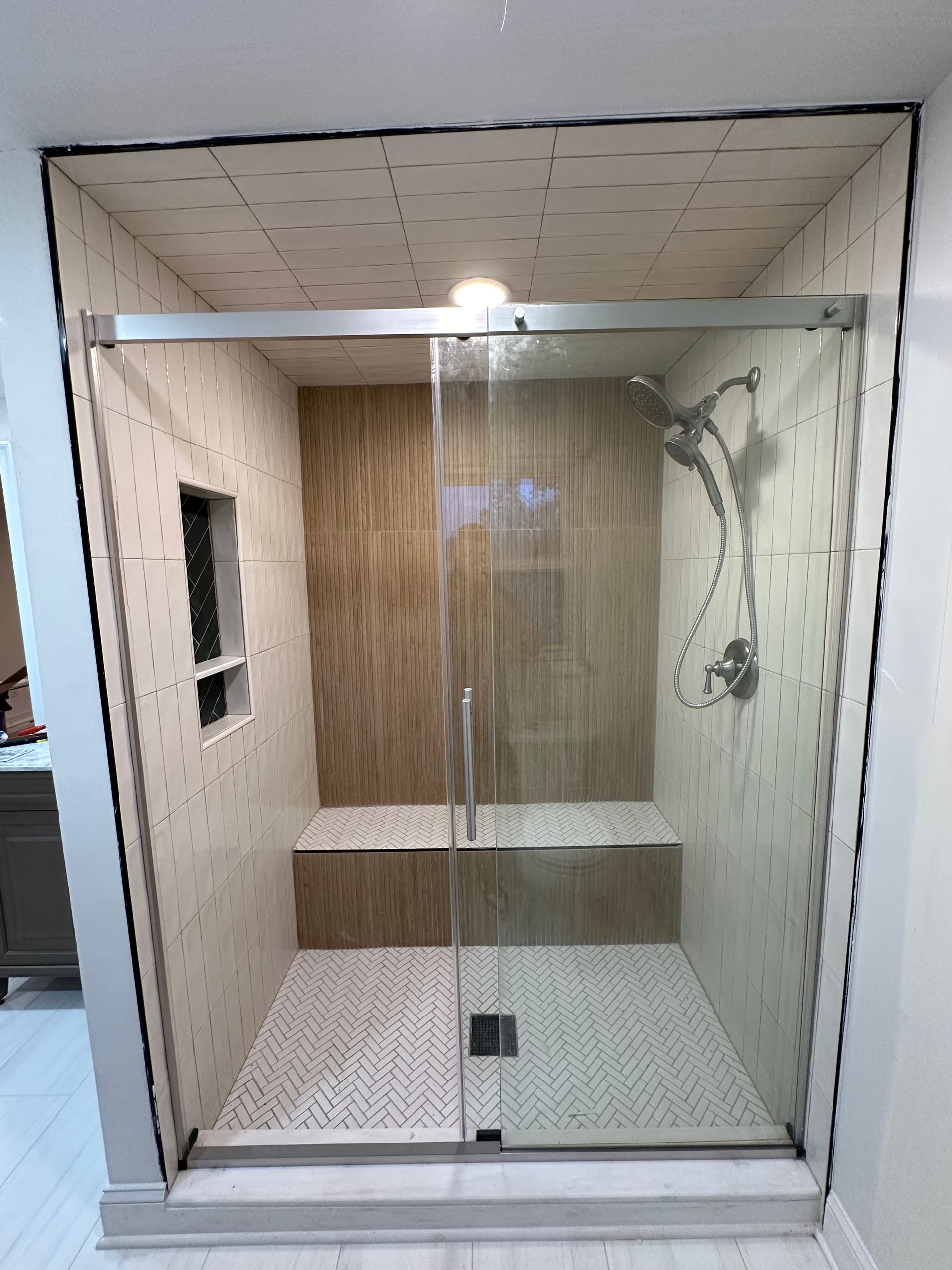 A bathroom with a sliding glass shower door and a bench.