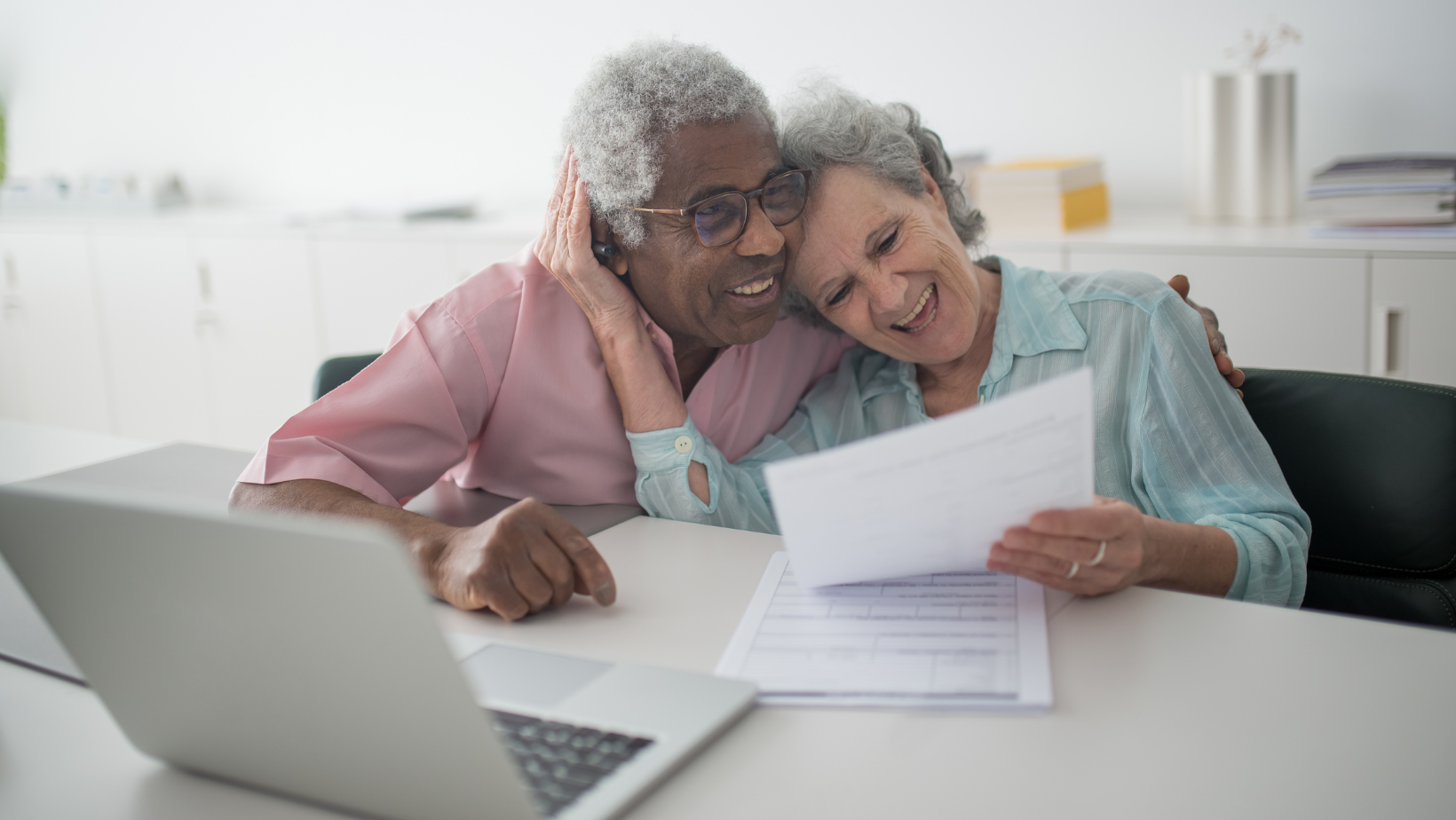 Two people reviewing papers together at a laptop in a bright office