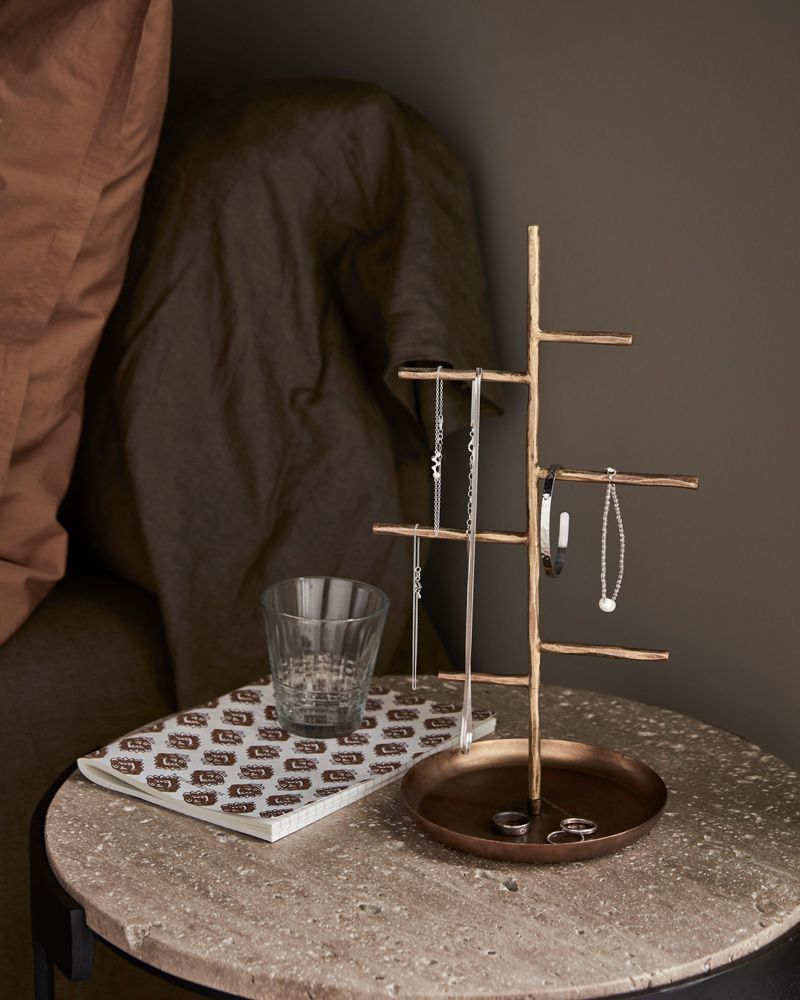 Decoratieve sieradenstandaard op een glinsterend rond dienblad naast een glas op een wit tafelkleed.