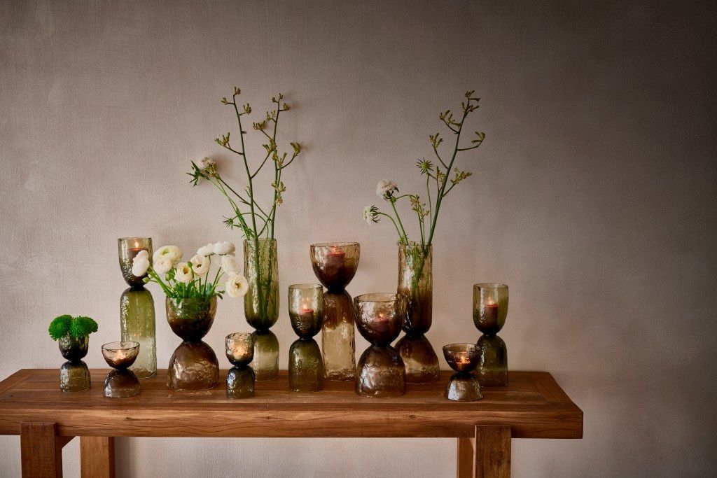 Glazen vazen gevuld met bloemen staan op een houten tafel tegen een neutrale muur.