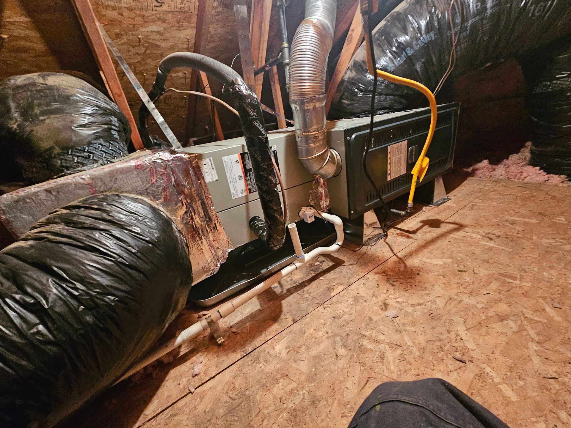 A person is sitting in an attic with a heater and a hose.