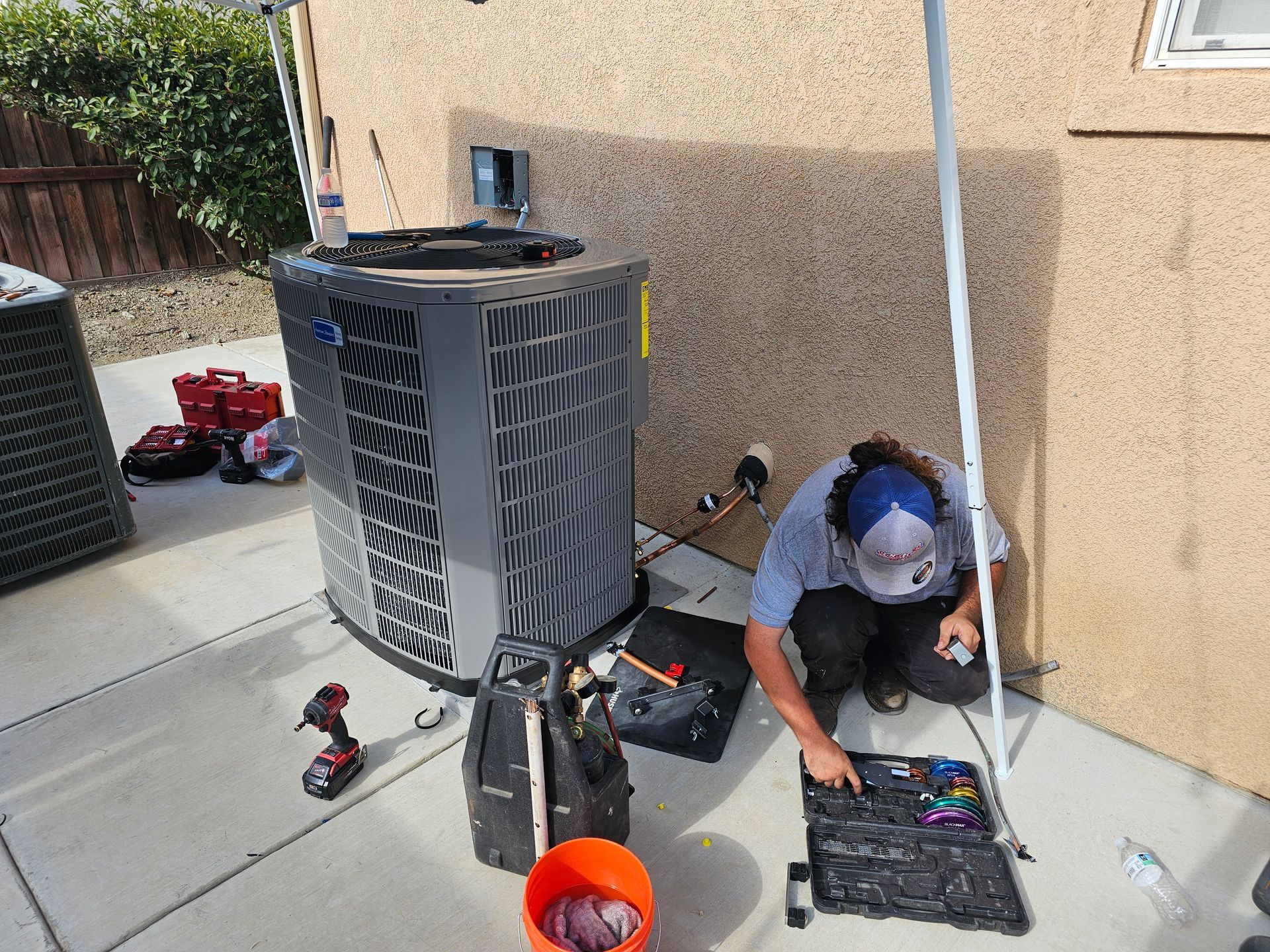 A man is working on an air conditioner outside of a house.