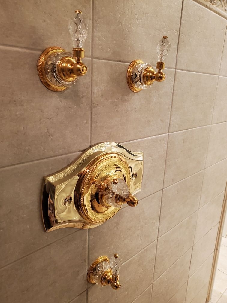 New gold-finish shower trim with clear decorative handles and a broad plate around the main control after valve replacement.