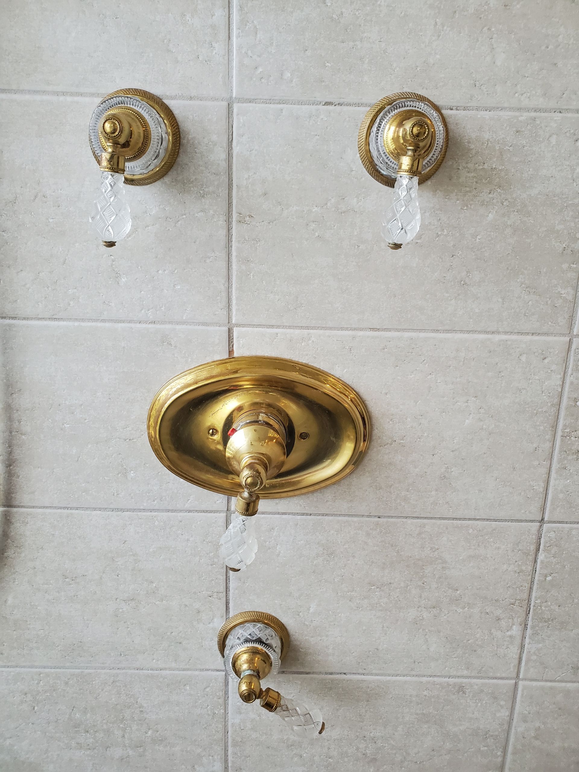 Original gold-finish shower controls with clear decorative handles and an oval central trim plate.