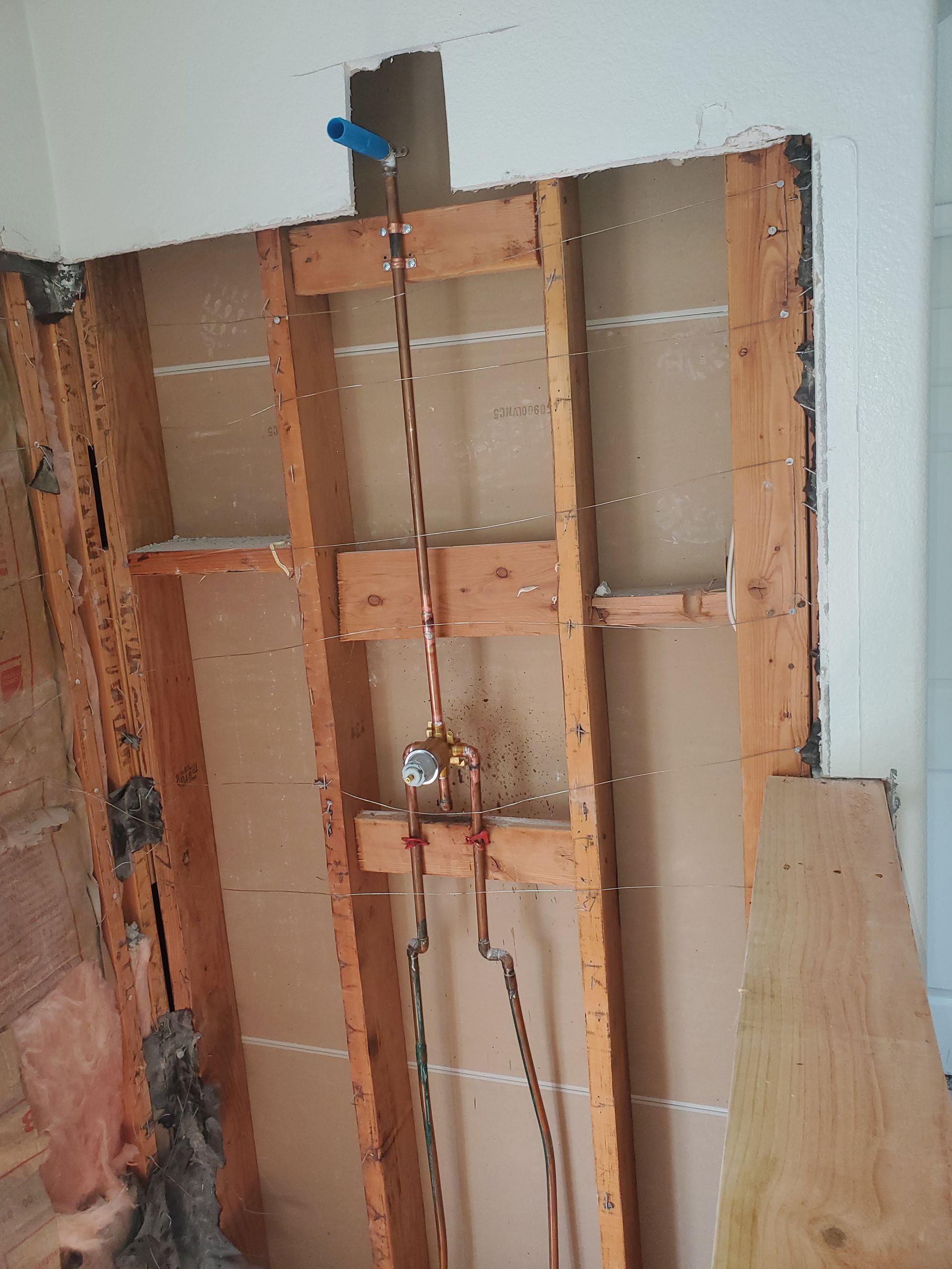Open shower wall with copper supply lines, a central valve, a vertical riser, and a secured upper outlet.