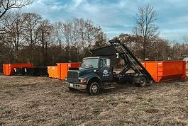 A dump truck is parked in a field with orange dumpsters.