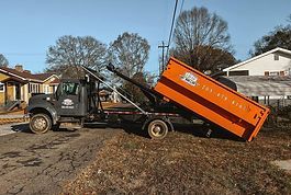 A dumpster is being towed by a dump truck.