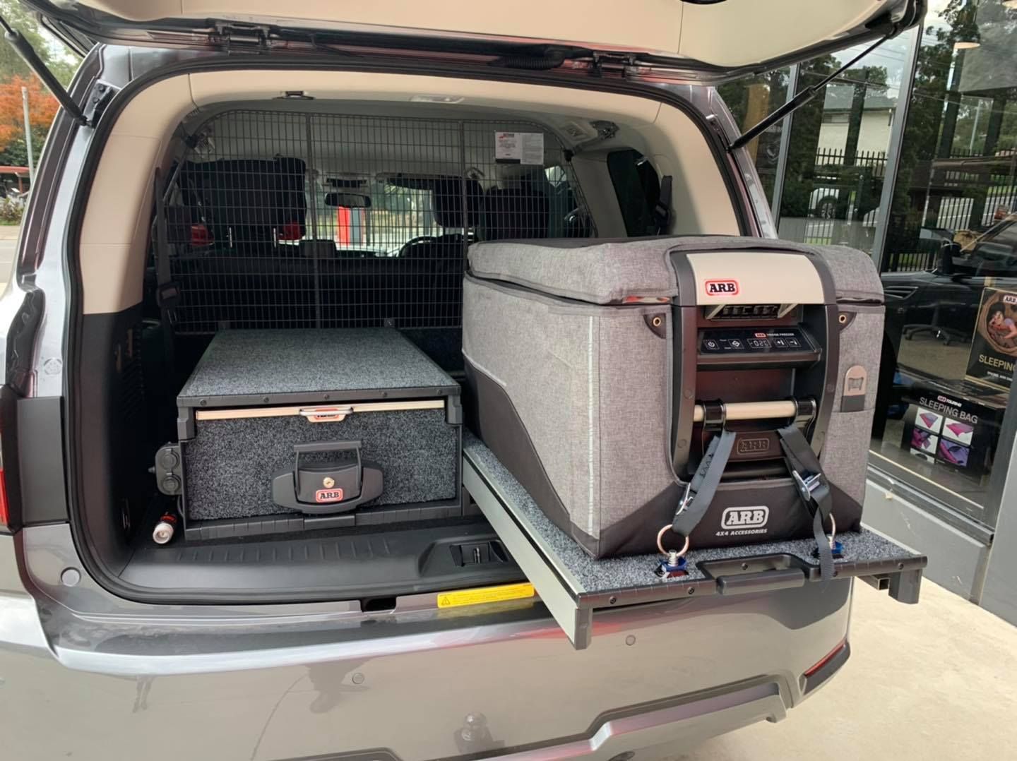 Open SUV trunk with camping/storage gear, including a gray drawer unit and black case behind a mesh barrier — Ol Mate 4x4 in Tuggerah, NSW