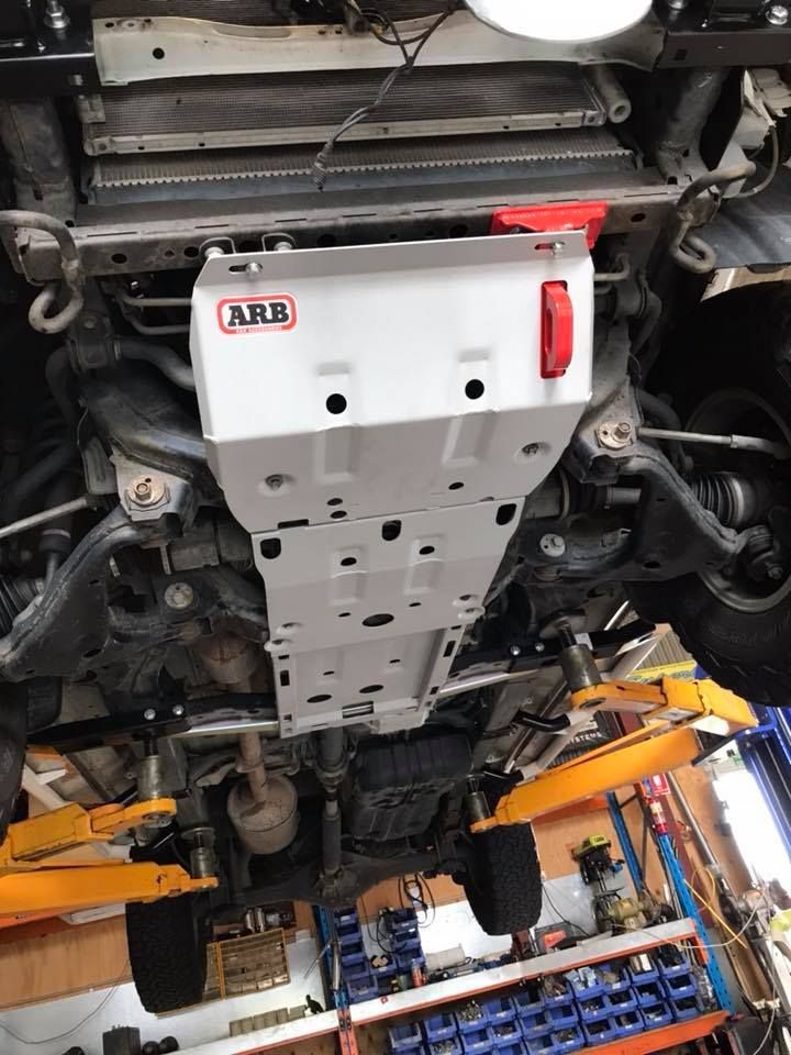 Underbody view of a car on a lift with a white skid plate and yellow support arms in a garage — Ol Mate 4x4 in Tuggerah, NSW