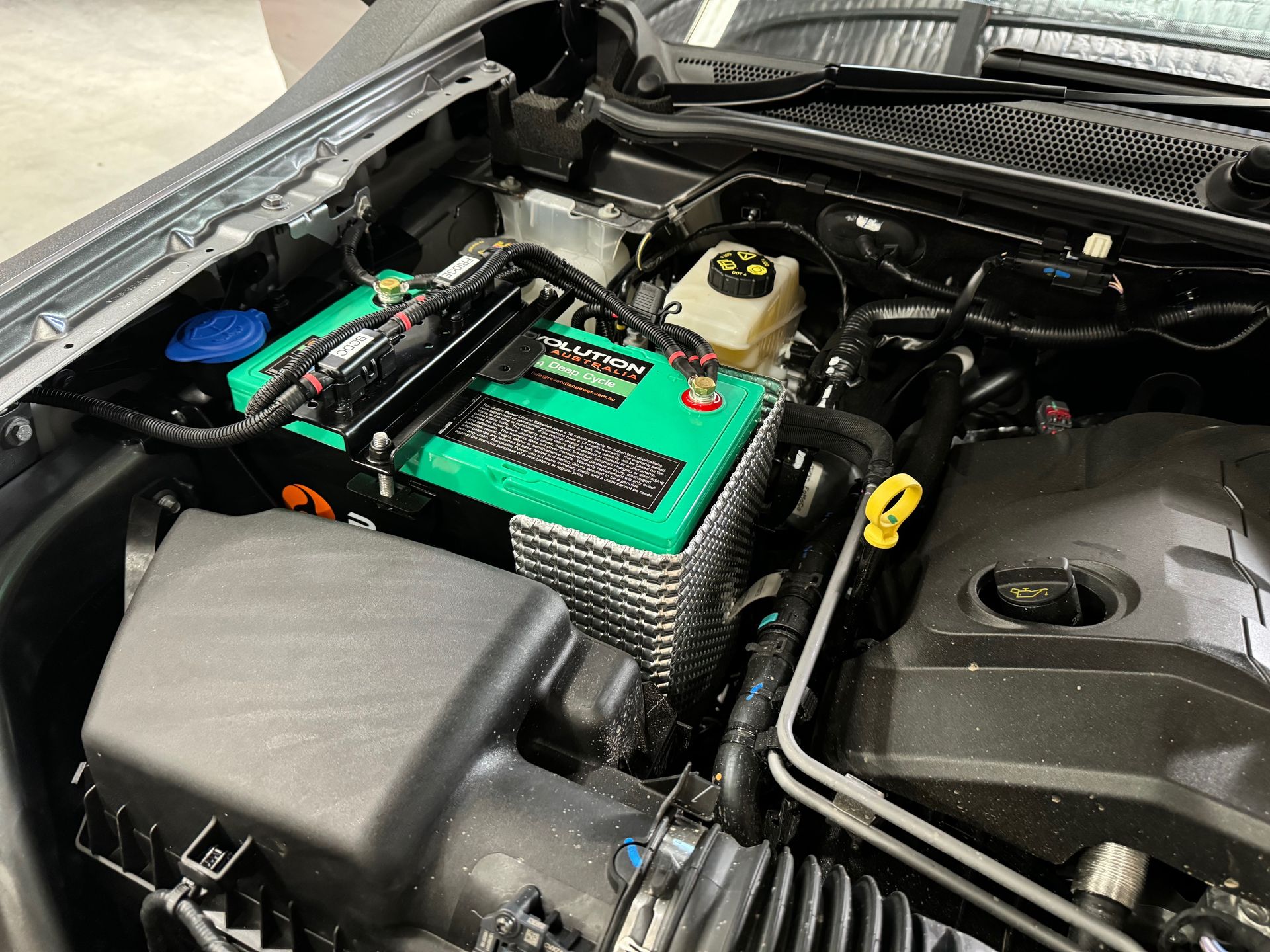 Car engine bay with a bright green and black battery pack mounted near the firewall — Ol Mate 4x4 in Tuggerah, NSW