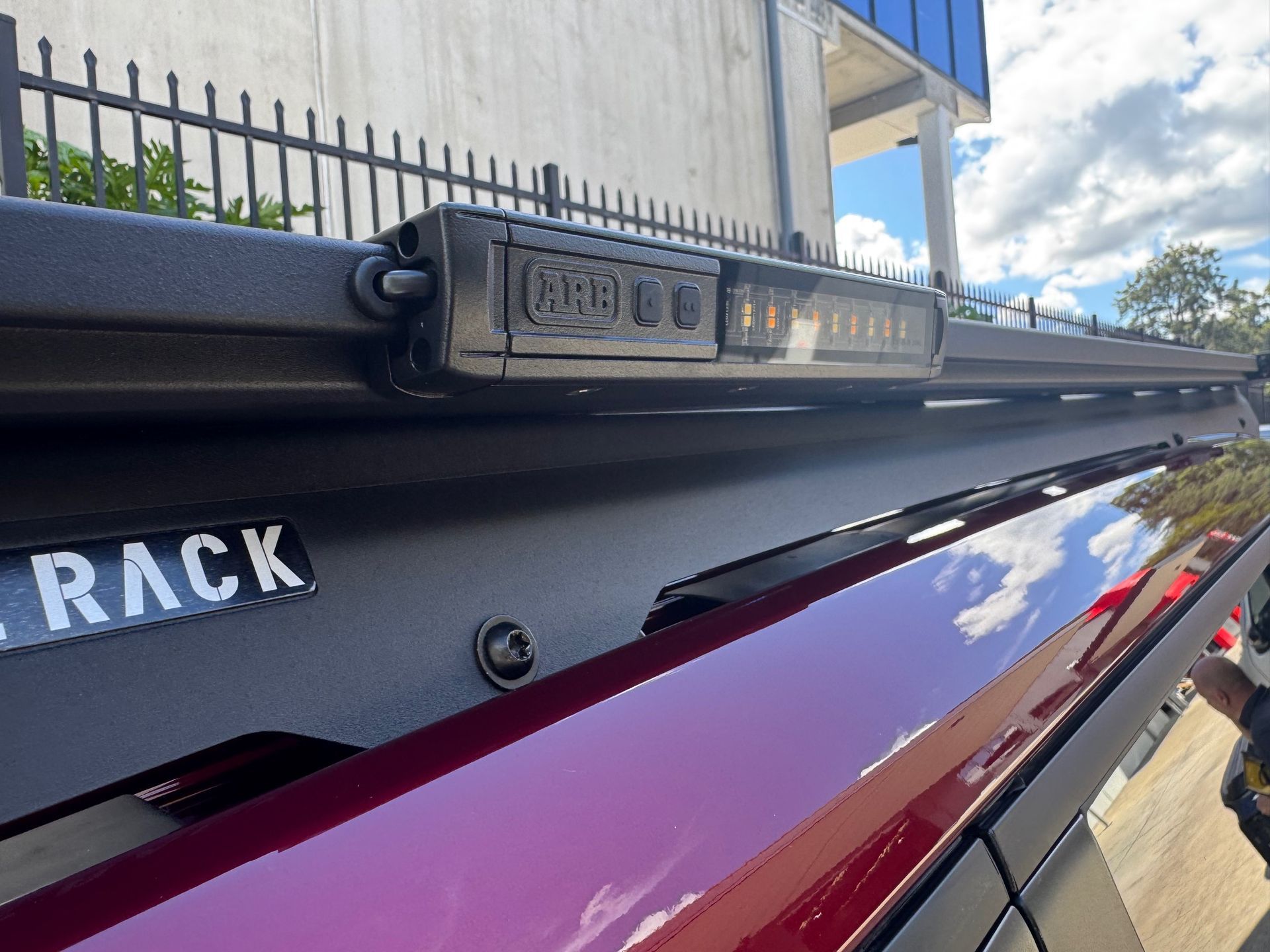 Close-up of a black roof rack mounted on a red vehicle, with a building and sky in the background — Ol Mate 4x4 in Tuggerah, NSW