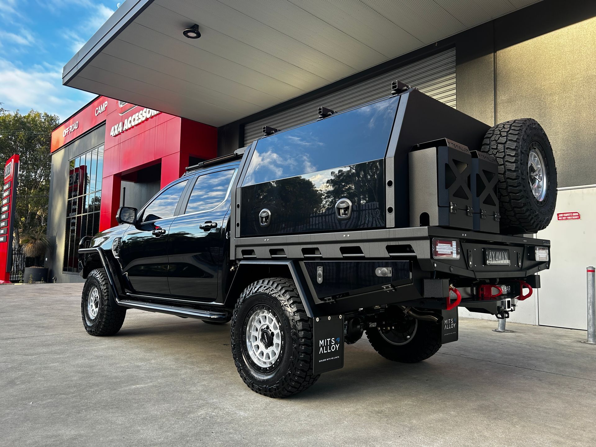 Black lifted pickup truck parked outside a red auto shop, rear view with spare tire and canopy — Ol Mate 4x4 in Tuggerah, NSW