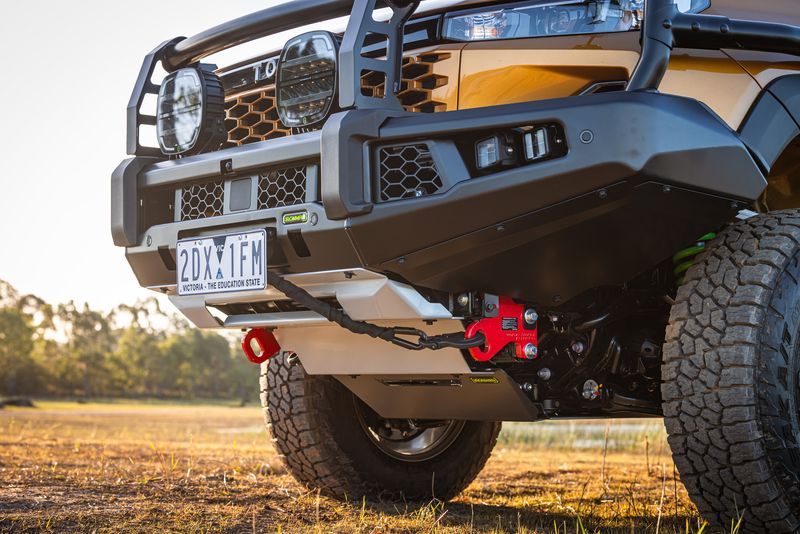 Front view of a lifted off-road truck with a winch bumper, red tow hook, and large tires on a field — Ol Mate 4x4 in Tuggerah, NSW