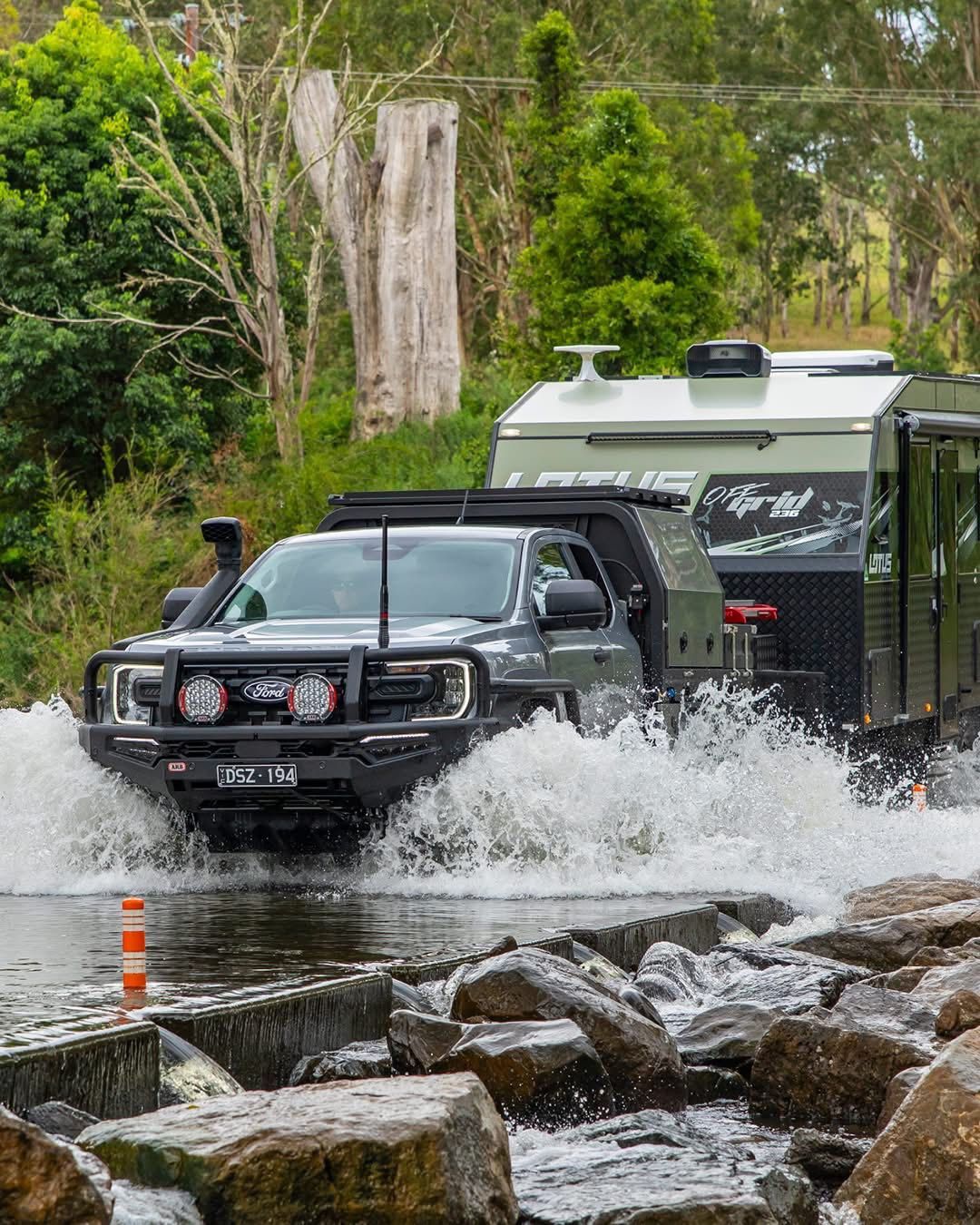 Black off-road truck drives through floodwater in a wooded area, splashing heavily — Ol Mate 4x4 in Tuggerah, NSW