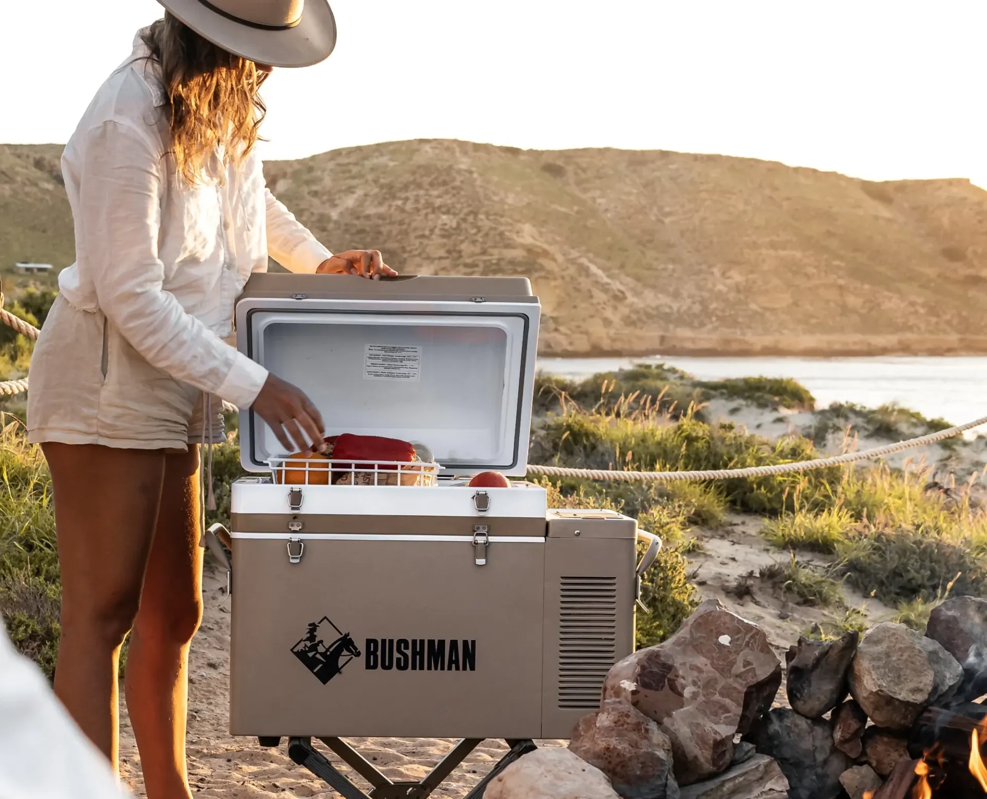 Person loading a gray Bushman cooler outdoors by a rocky riverbank at sunset — Ol Mate 4x4 in Tuggerah, NSW
