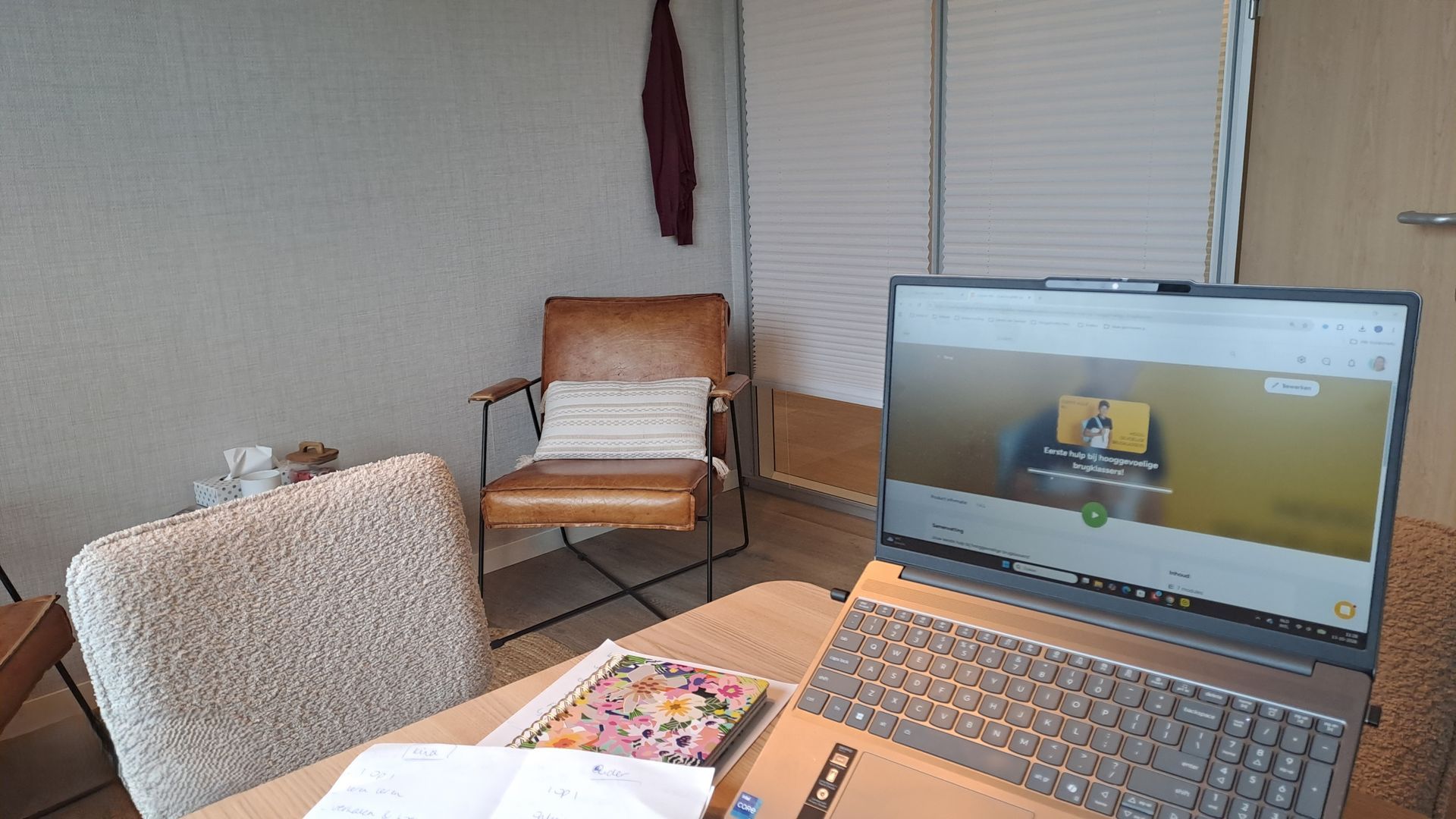 Laptop op een tafel in een gezellige kamer, met stoelen en een jaloezie op de achtergrond