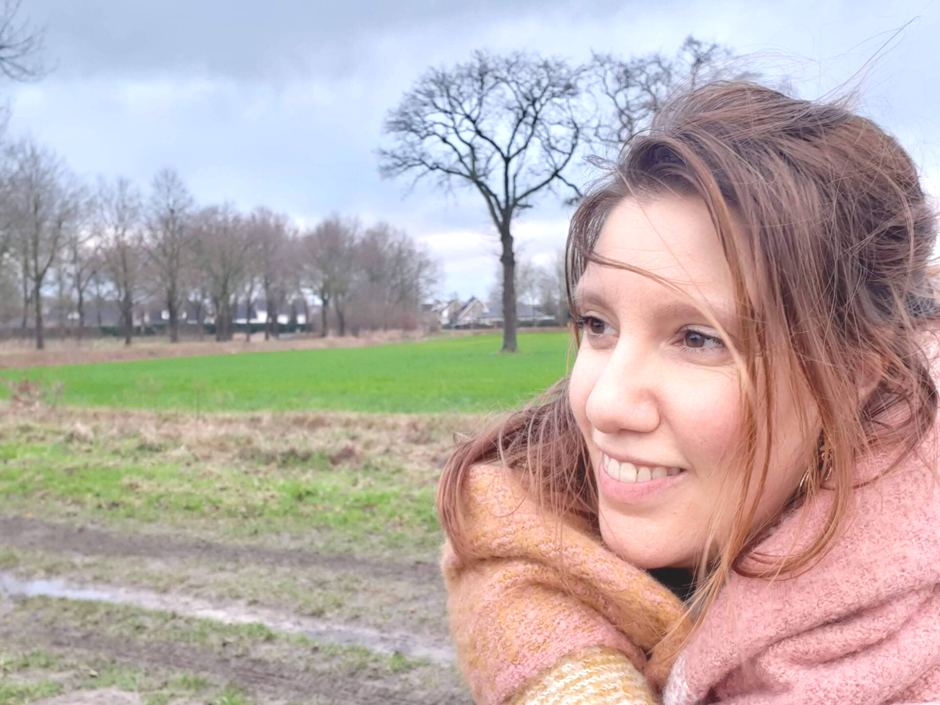 Joyce glimlacht in de buitenlucht. Op de achtergrond zijn een veld en bomen te zien.