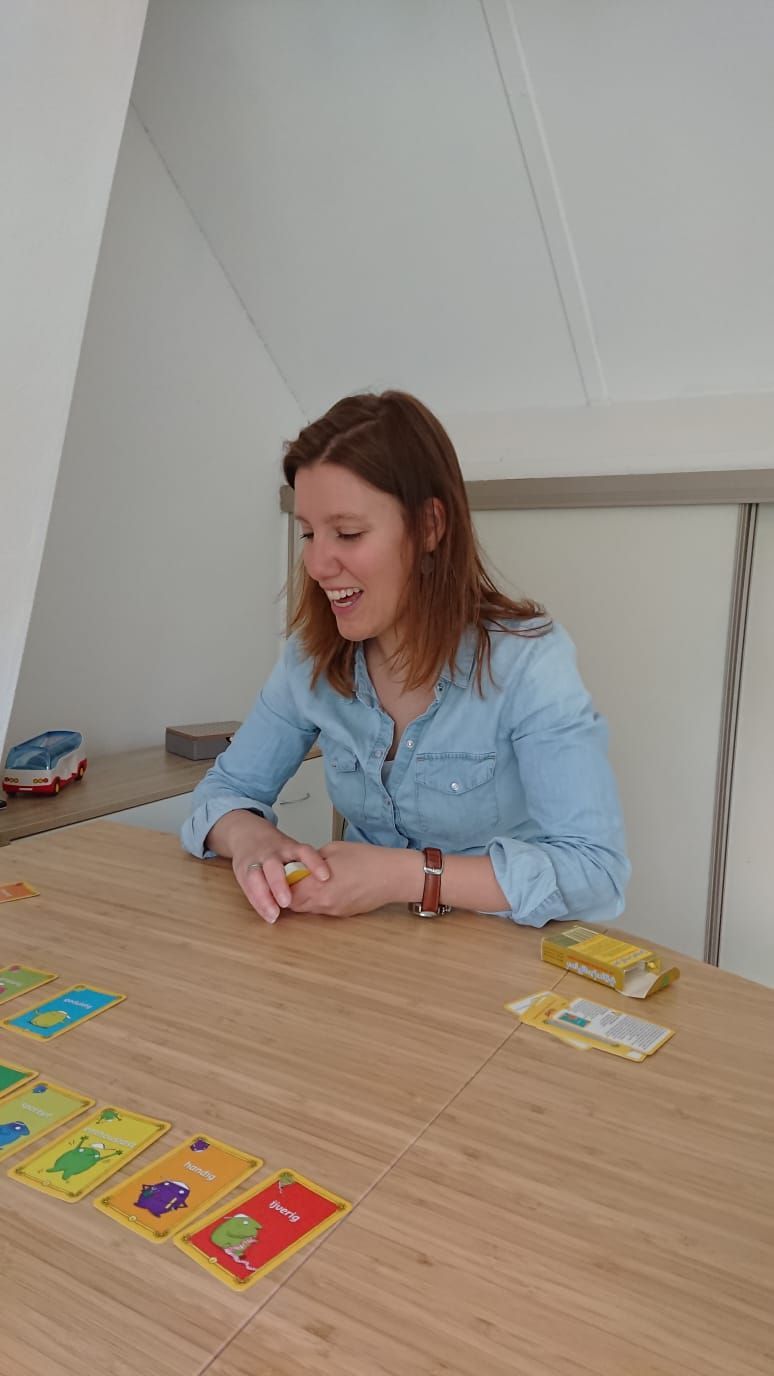 Een vrouw lacht terwijl ze een kaartspel speelt aan een houten tafel in een felverlichte kamer.