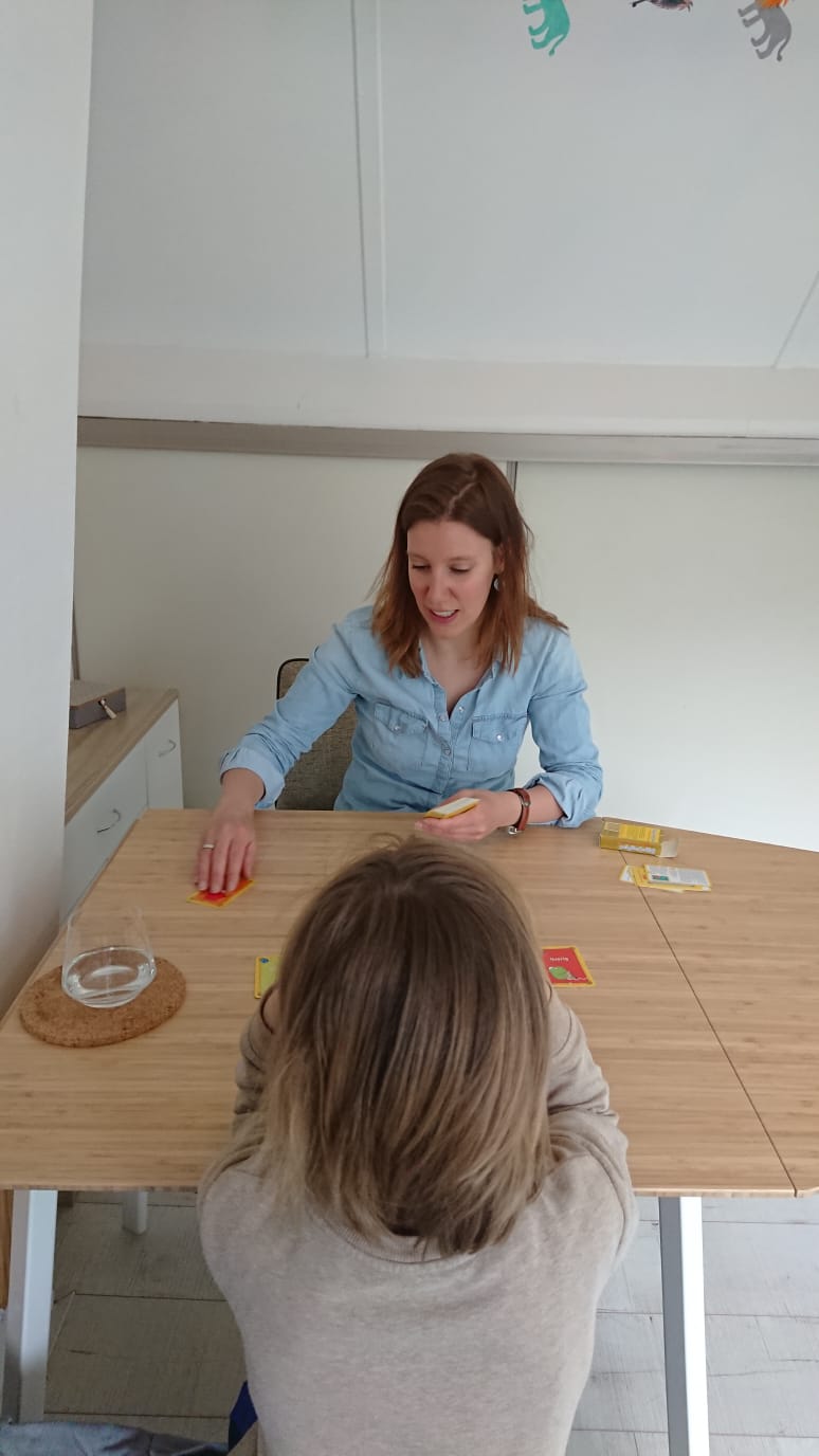 Een vrouw en een kind spelen een spel aan een tafel met kaarten en cijferblokken.