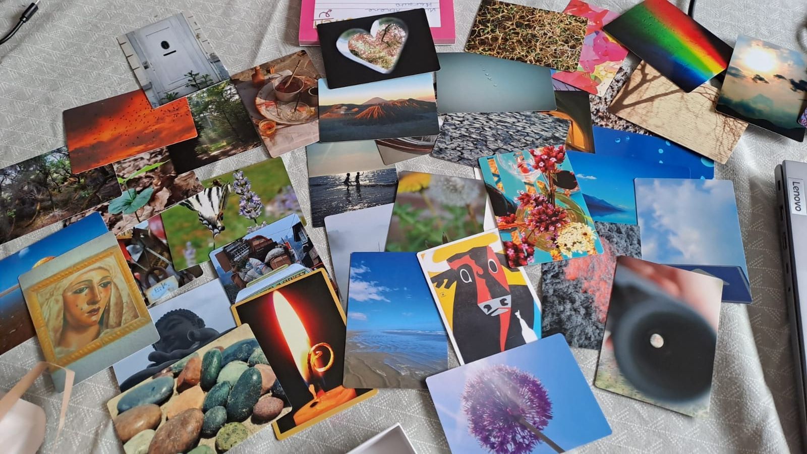 Verspreid over een deken liggen kleurrijke fotoafdrukken, met landschappen, abstracte kunst en een zwart rond voorwerp