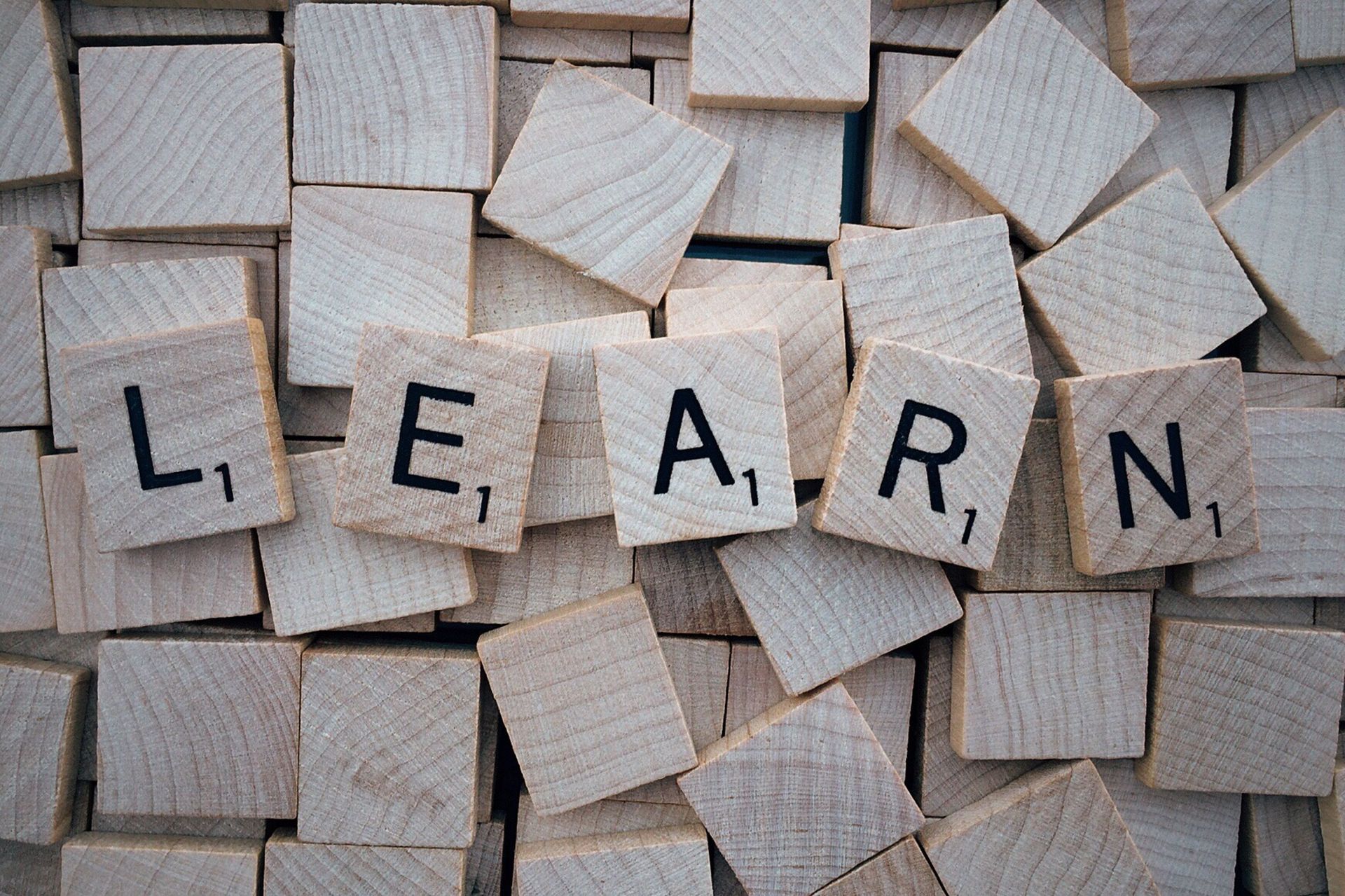 Houten letterblokjes die samen ‘LEARN’ vormen, tussen verspreide blokjes