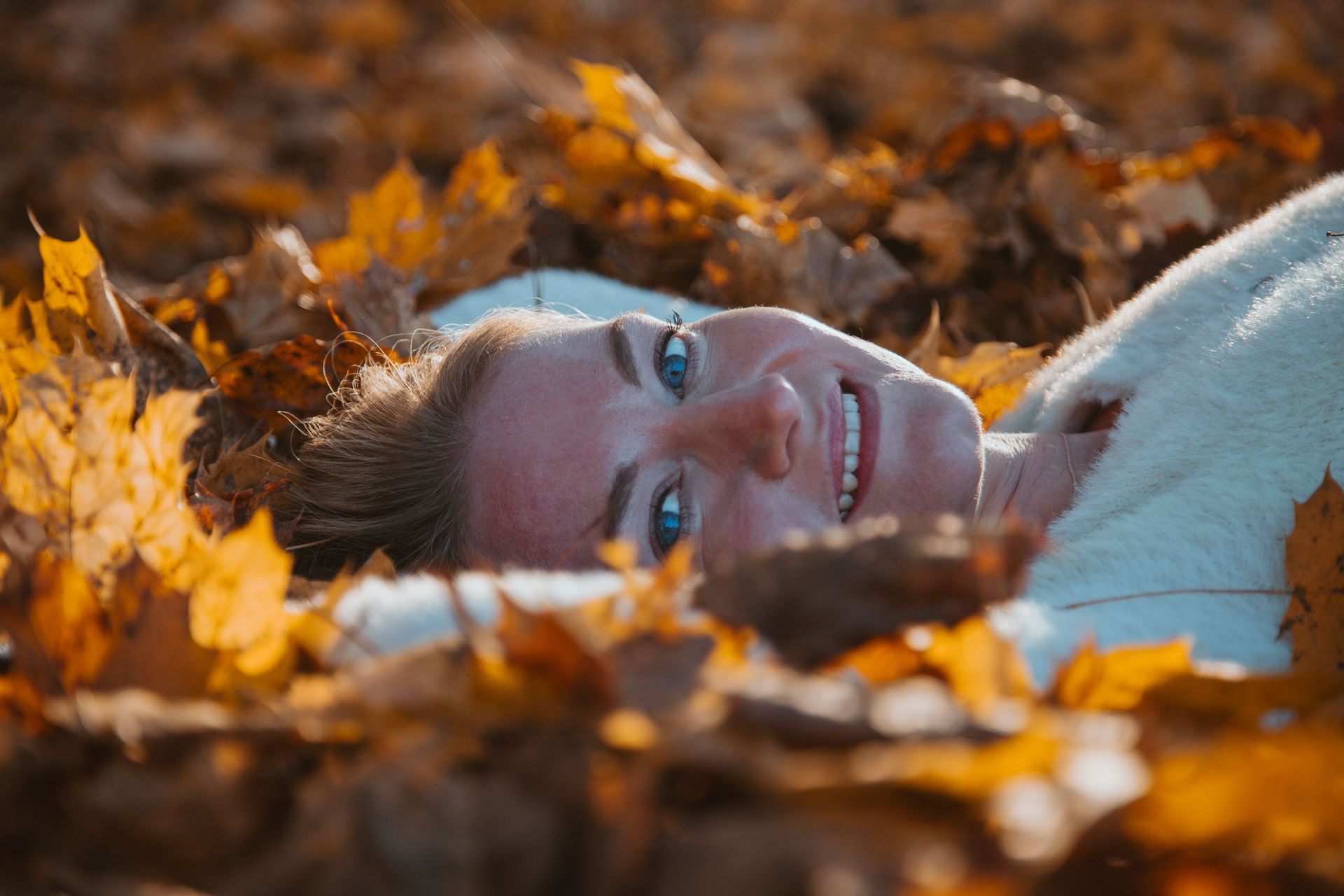 Jongen met blauwe koptelefoon luistert naar muziek in een park met herfstbladeren.